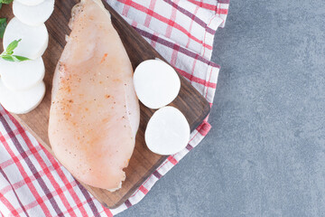 Uncooked chicken fillet with radish slices on wooden board
