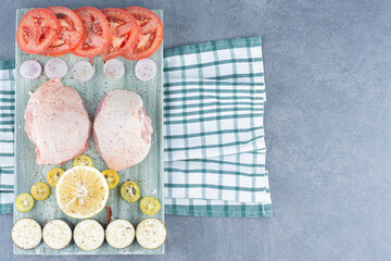 Two chicken fillets and sliced vegetables on wooden board