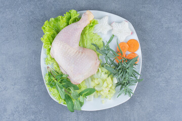Raw chicken legs with vegetables on white plate
