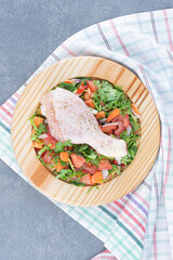Raw chicken drumstick and sliced vegetables on wooden plate