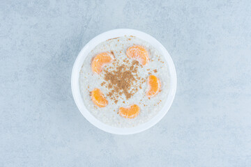 Orange slices and cinnamon powder on top of porridge in a bowl, on the marble background