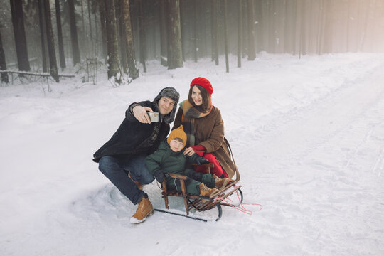 Happy family taking selfie while walking in a snowy forest. Parents with their little son sledding on a snowy day. Merry Christmas holidays.