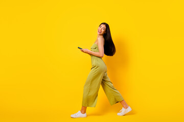Fototapeta na wymiar Full size profile portrait of lovely cheerful vietnamese lady hold telephone walk isolated on yellow color background