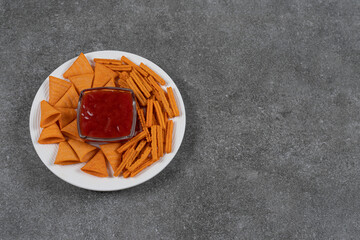 Ketchup, corn chips and dried bread on plate , on the marble background