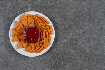 Ketchup, corn chips and dried bread on plate , on the marble background