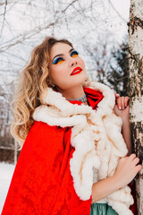 A girl in red clothes leans on a birch winter snow