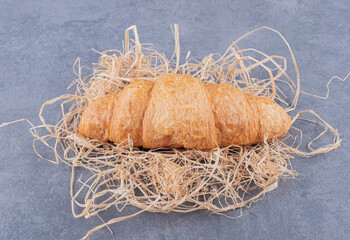 Close up photo of Fresh French croissant on straw over grey background
