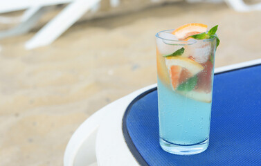Glass of refreshing drink with grapefruit and mint on blue lounger at beach, space for text
