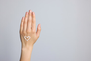 Heart painted with cream on hand against light grey background, closeup. Space for text