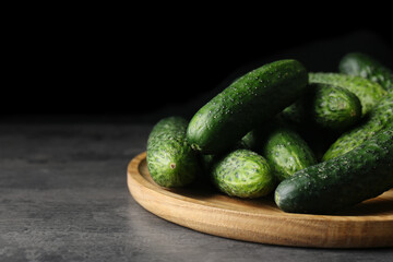 Wooden board with fresh ripe cucumbers on dark grey table, space for text