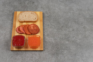Pepperoni slices, rye bread and sauces on wooden board