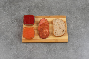 Pepperoni slices, rye bread and sauces on wooden board
