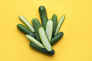 Whole and cut fresh cucumbers on yellow background, flat lay
