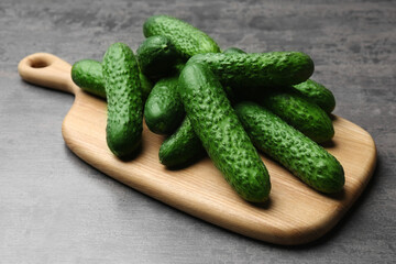 Wooden board with fresh ripe cucumbers on dark grey table