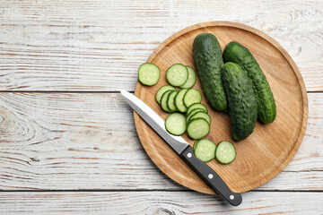 Whole and cut fresh ripe cucumbers on white wooden table, flat lay. Space for text