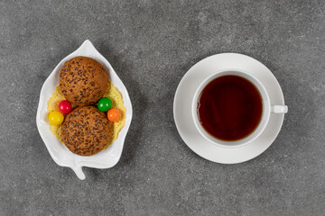 Cookies with candies on white plate and cup of tea