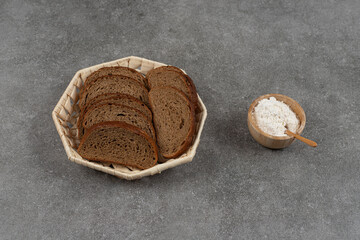 Black bread slices in wooden basket with bowl of flour
