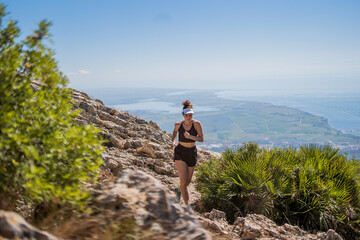 Naklejka premium Blonde caucasian woman with a visor running on top of a mountain with a view