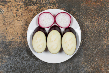 Radish and eggplant in the plate, on the marble background