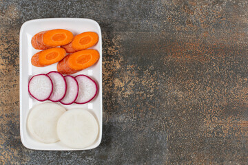 Raw carrot, white and red radish on the plate , on the marble background