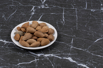 Flavorful shelled almonds in the plate , on the marble background