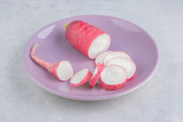 Fototapeta na wymiar Ripe sliced of radish on the pink plate, on the blue background