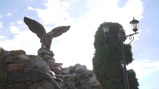 Decorative waterfall on natural stones with eagle statue fnd blue sky. Slowmo