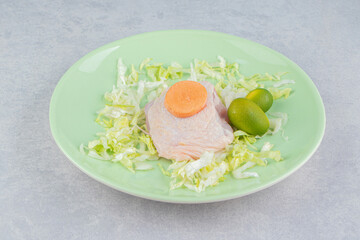 Chicken meat on the greens with kumquat and carrot on the plate, on the white background