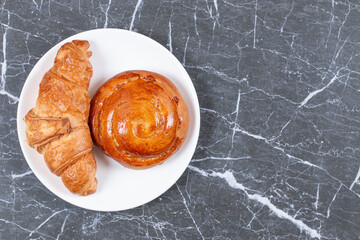 Bun and chocolate croissant on the plate, on the marble background