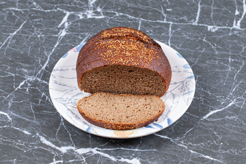 Tasty black bread with sesame on the plate , on the marble background