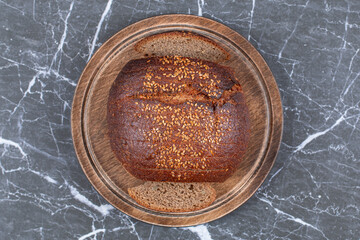 Black bread with sesame on the wooden plate , on the marble background