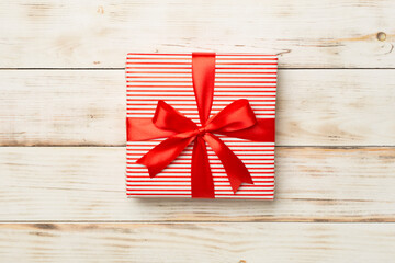 Gift box with red ribbon bow on wooden background, top view