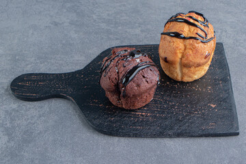 A dark wooden board with two sweet muffins