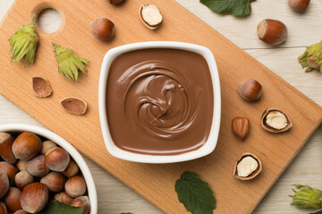 Hazelnut cream with nuts and green leaves on wooden background, top view