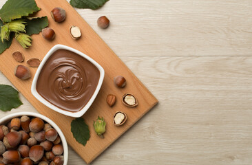Hazelnut cream with nuts and green leaves on wooden background, top view