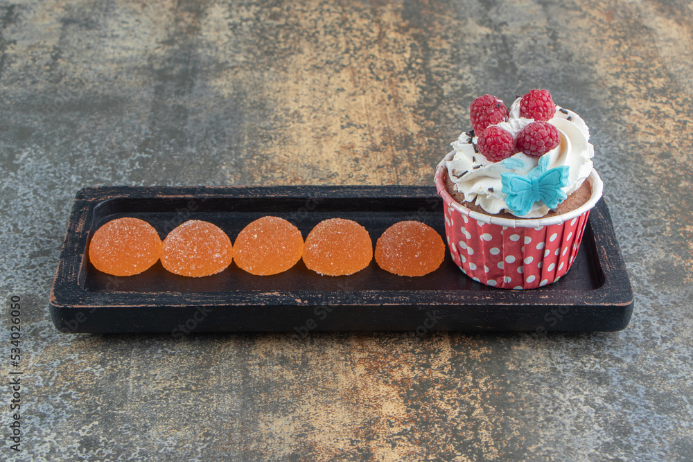 Wall mural Tasty cupcake decorated with cream and candies on black plate