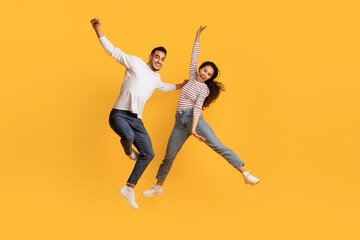 Playful Mood. Happy Middle Eastern Couple Jumping In Air Over Yellow Background