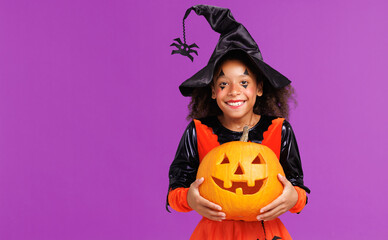 Happy cheerful ethnic girl in a pumpkin costume celebrates Halloween and laughs on a bright purple...