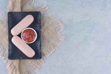 Fresh organic sausage with ketchup on black plate