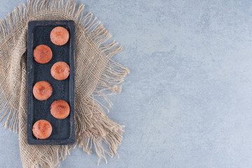 Fried sausage slices on black wooden plate