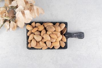 A tray of almonds next to leaves, on the marble background