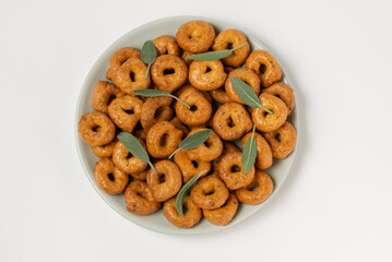 Traditional italian snacks taralli or tarallini with sage leaves in plate isolated on white background, top view