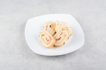 A sliced of roll cake in the plate, on the marble background
