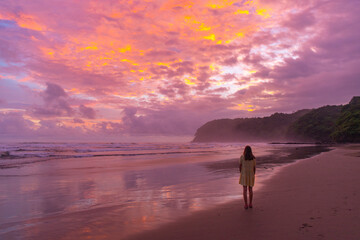 Naklejka premium pretty girl in dress watching unique pink colorful sunset on the beach in costa rica, pacific coast - playa san miguel