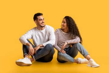 Portrait of beautiful young middle eastern couple sitting together over yellow background