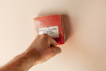 Male fist breaks plastic cover of red fire alarm button