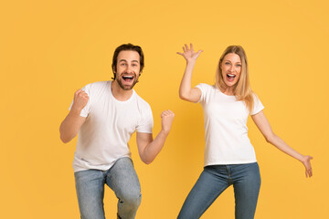 Glad young caucasian woman and male in white t-shirts dance, enjoy victory and success, make win...
