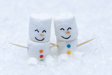 A pair of marshmallow snowmen sit in the snow.
