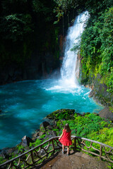 rear view of a beautiful girl in red dress watching blue waterfall in costa rica; volcan tenorio...