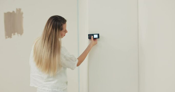Interior designer walks around property for sale uses distance meter to measure amount of paint needed to paint apartment.